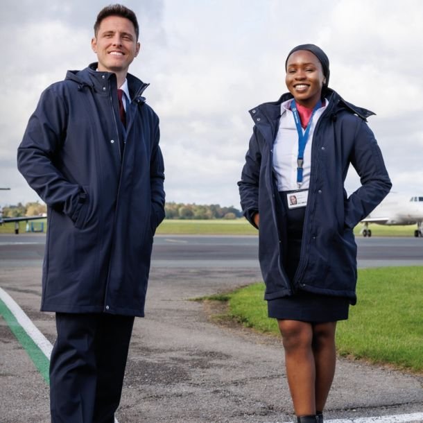 Man and woman each wearing airline soft-shell coat in front of aircraft.